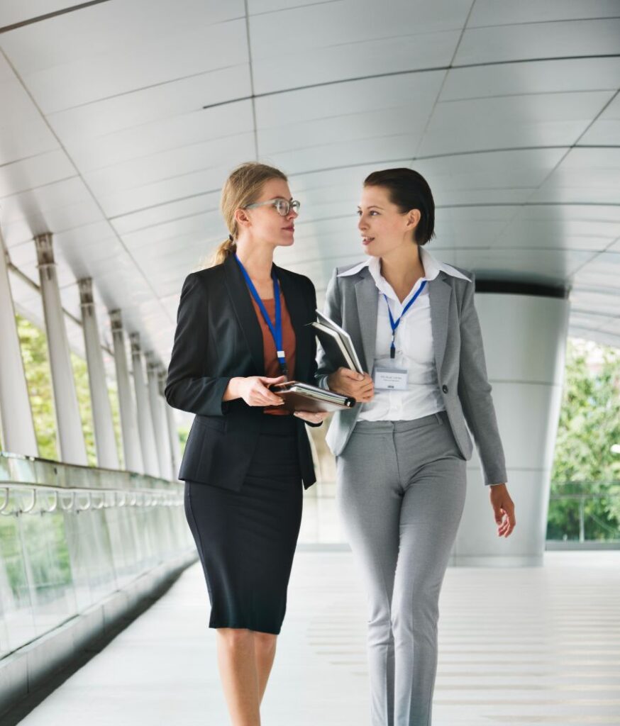 two professional women walking down a hallway in a corporate building.