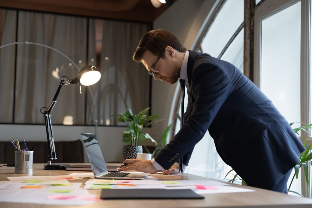 man in a suit standing over a desk in an office