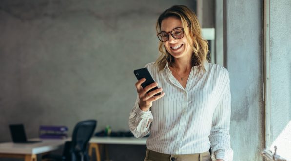 a woman standing in an office looking at her phone and smiling