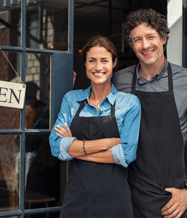 Two small business owners standing in front of their shop smiling.